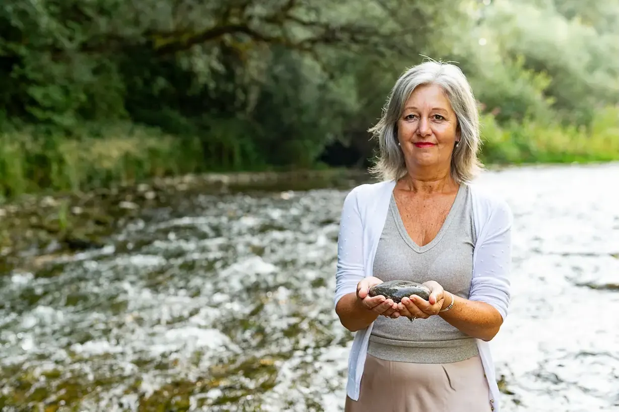 Martina Sedlmair steht an einem Fluss und hält einen Stein in beiden Händen